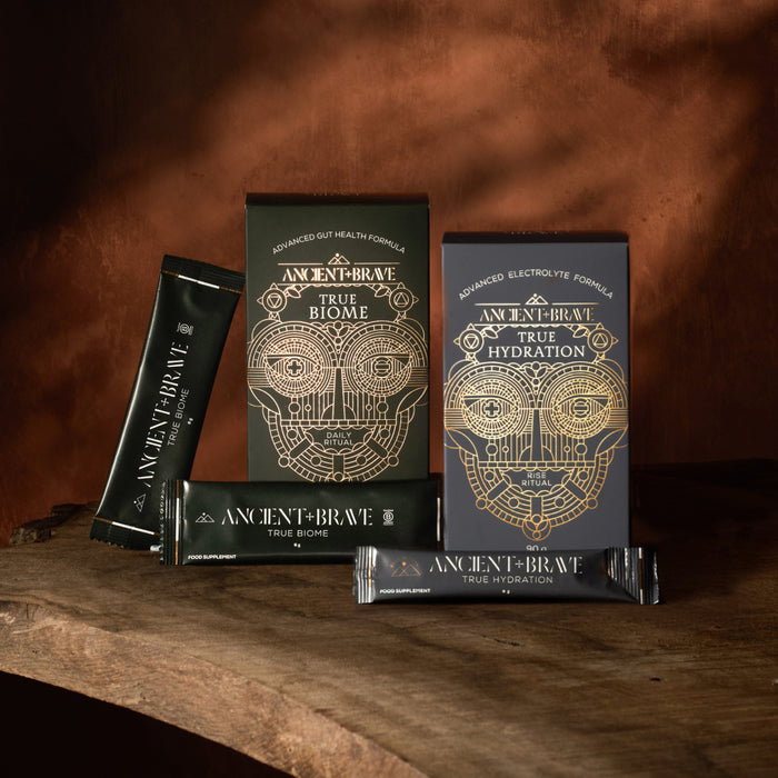 Ancient Brave True Biome and True Hydration sachets and boxes on a wooden surface with a warm brown background