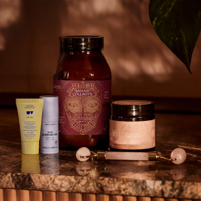 Jar of Radiant Collagyn, True Skin Alchemy, Ultra Violette SPF 50+, The Support Oil and skin roller on a reflective surface with a warm background.
