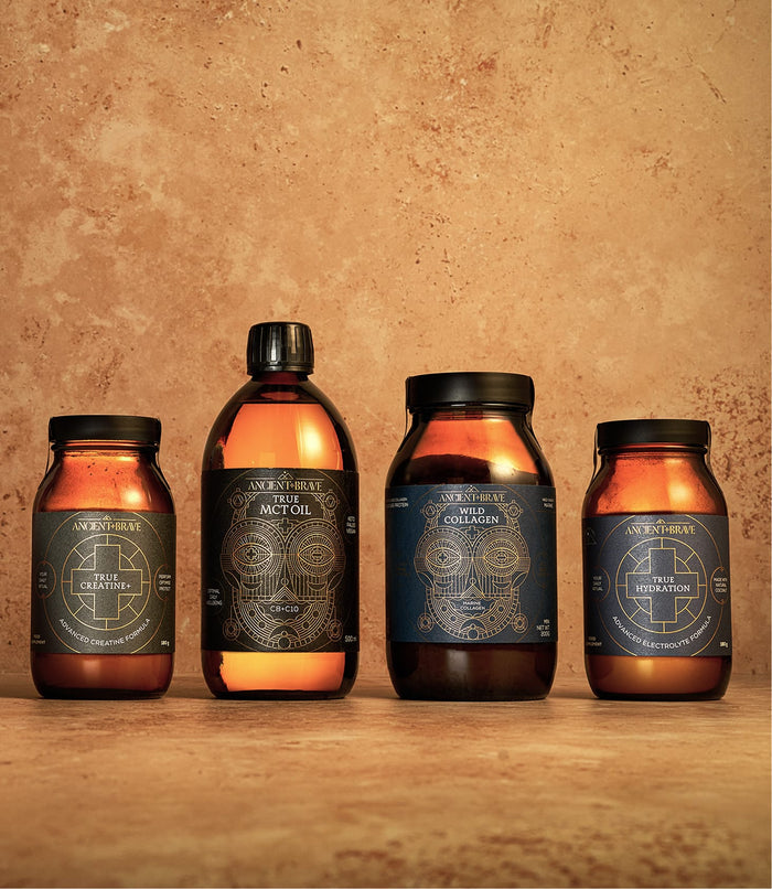 Four amber jars and bottles with intricate geometric labels from Ancient + Brave’s Ultimate Workout Kit—creatine supplement, MCT oil, collagen peptides, and hydration powder with electrolytes—are displayed against a textured, earthy brown background.