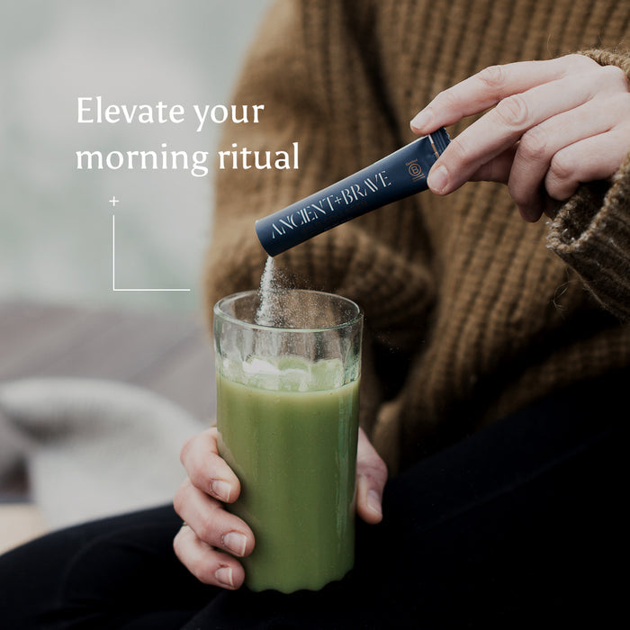A person in a brown sweater pours Wild Collagen Sachets, rich in hydrolysed collagen, into a glass of green drink. The text reads: Elevate your morning ritual.