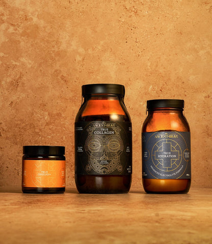 Three amber jars of the Ancient + Brave Beauty Kit supplements rest on a brown stone surface and background. Each jar features a uniquely designed label—one orange, one black with gold, and one dark blue with silver—and is expertly formulated to support hair growth, enhance skin elasticity, and promote overall wellness with the power of collagen peptides.