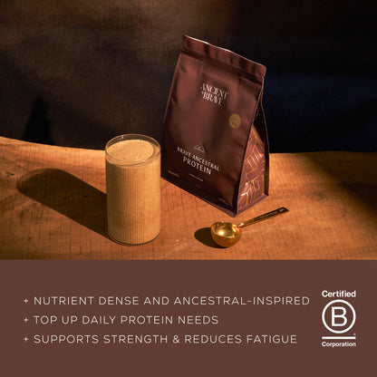 Glass of protein shake next to a bag of 'Ancient + Brave' ancestral protein powder on a wooden surface with a dark background. With product benefits text: nutrient dense and ancestral-inspired, top up daily protein needs, supports strength and reduces fatigue.