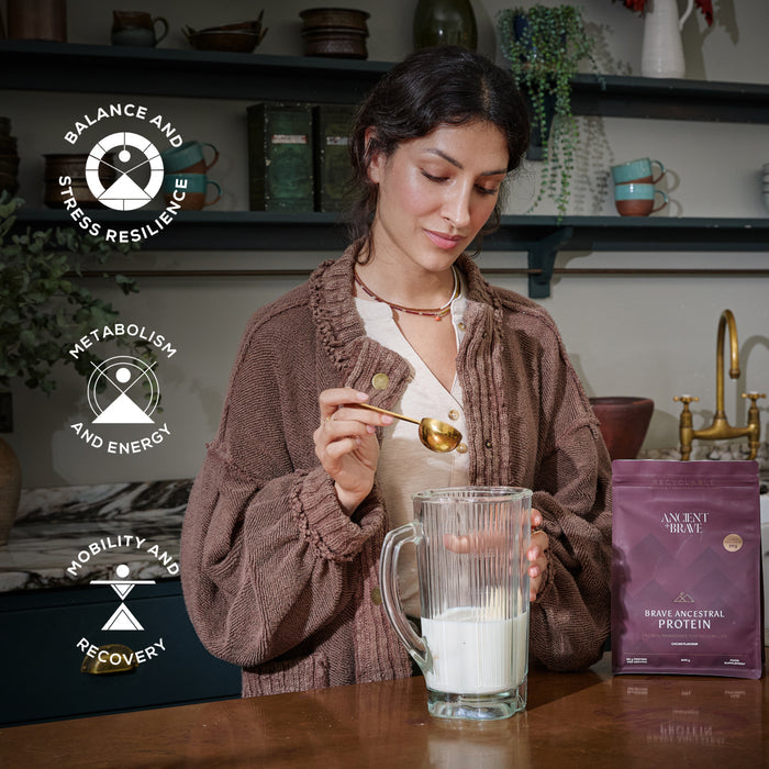Woman preparing a protein shake with a package of Ancient + Brave's protein powder in a kitchen setting. With three symbols 'balance and stress resilience', 'metabolism and energy' and 'mobility and recovery'