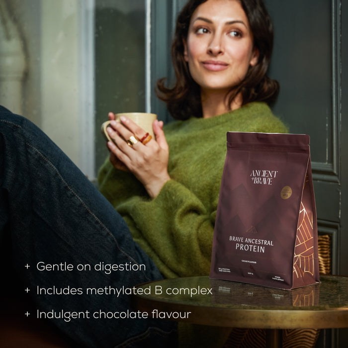 Woman holding a mug with a pouch of Brave Ancestral Protein on a table. With text below 'gentle on digestion'.