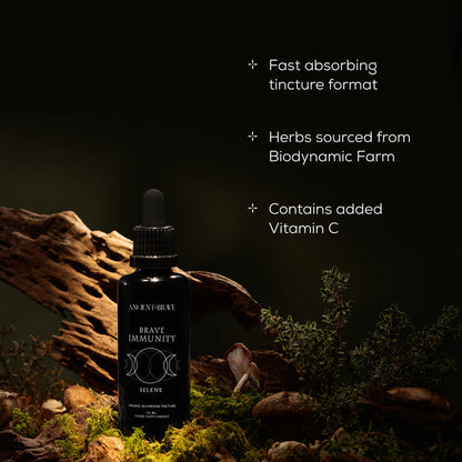 A dark glass dropper bottle labeled Brave Immunity by Ancient + Brave rests on mossy wood; text emphasizes its fast-absorbing tincture, organic botanicals and herbs sourced from a biodynamic farm, added Vitamin C, and functional mushrooms to support immune strength—all showcased against a striking black background.
