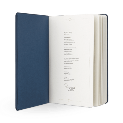 An open navy blue hardcover Brave Tinctures Trio Set by Ancient + Brave is displayed with a printed poem on cream-colored pages, featuring a small decorative leaf illustration beneath the text. The white background evokes an atmosphere of clarity and calm.