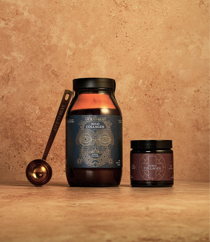 Two jars from the Collagen Expert Kit by Ancient + Brave—one large and one small—rest on a tan textured surface. A metallic measuring spoon lies nearby. The deep blue and purple labels, adorned with gold geometric designs, highlight Type I and Type II collagen for advanced joint support.