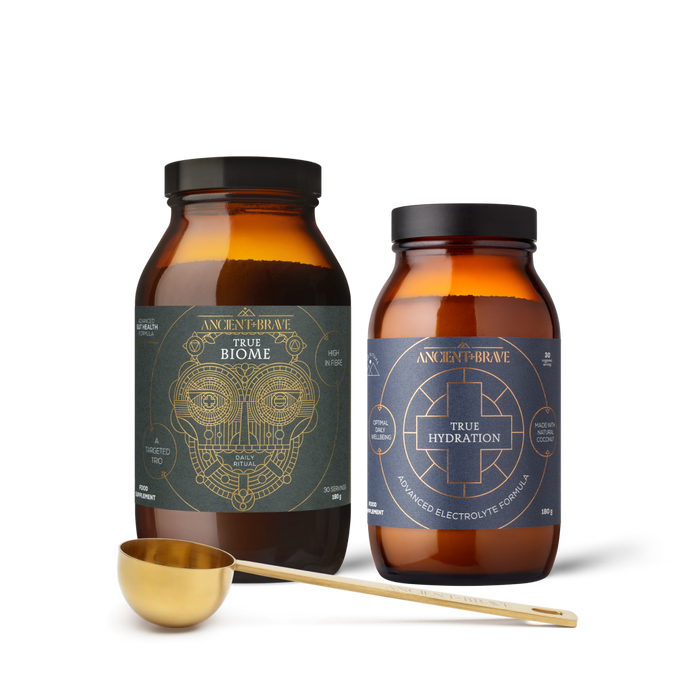 Two bottles of 'True Biome' and 'True Hydration' with a gold scoop on a white background