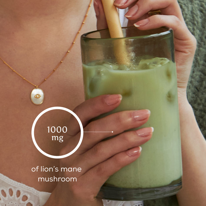 A person enjoys a glass of iced green drink with a straw. Overlay text reads: 1000 mg of Lion’s Mane mushroom. They wear a gold necklace and have neatly manicured nails, savoring the refreshing blend made with Ancient + Brave Matcha + Collagen ceremonial grade matcha.