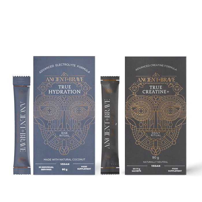 Two Ancient + Brave Recharge Ritual supplement boxes, each with matching stick sachets placed in front, display intricate geometric designs with gold and white text. Featuring an advanced electrolyte formula for enhanced muscle performance, Recharge Ritual is designed to elevate your daily routine.