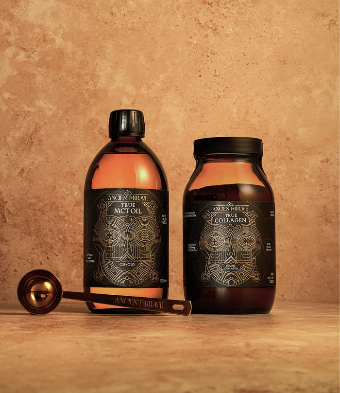 Two brown Ancient + Brave jars from The Beginner’s Kit, one labeled True MCT Oil and the other True Collagen, are placed on a stone surface with a metallic measuring spoon lying in front of them—essentials to support your wellness journey.