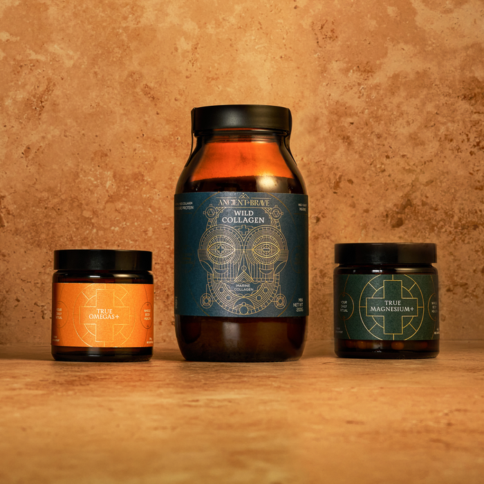 Three core supplements from Ancient + Brave’s The Foundation Kit are arranged on a tan stone surface: a large brown jar of hydrolysed collagen peptides at the center, with smaller jars of True Omega-3—rich in omega fatty acids—to the left and True Magnesium to the right.