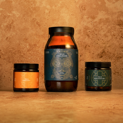 Three core supplements from Ancient + Brave’s The Foundation Kit are arranged on a tan stone surface: a large brown jar of hydrolysed collagen peptides at the center, with smaller jars of True Omega-3—rich in omega fatty acids—to the left and True Magnesium to the right.