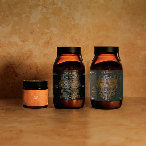 Three amber-colored supplement jars from Ancient + Brave, each with detailed geometric labels, are arranged on a tan surface. Designed to support gut health and immune balance as part of The Gut Health Kit, one small jar sits to the left of two larger jars—each featuring unique product names.