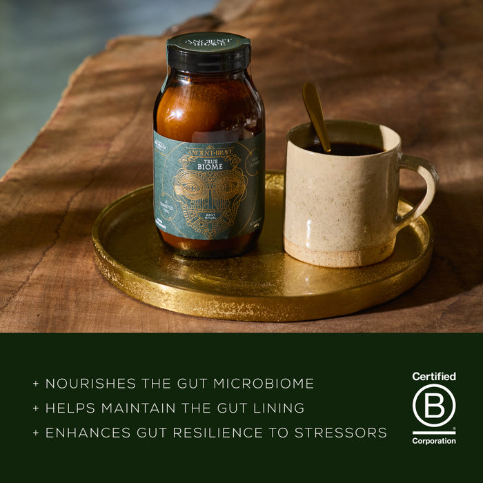 Jar of a product on a wooden surface with a cup and spoon, featuring a B Corp certification logo.