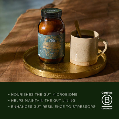 Jar of a product on a wooden surface with a cup and spoon, featuring a B Corp certification logo.
