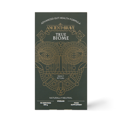 A sleek black box from Ancient + Brave, labeled “True Biome” and adorned with gold geometric patterns, features an advanced gut health formula containing prebiotics to support optimal gut barrier function. The packaging highlights it as a daily ritual, vegan-friendly, naturally neutral in flavor, and providing 30 servings.