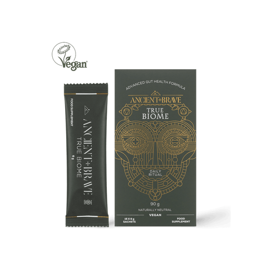 Ancient + Brave True Biome Sachets box and individual sachet, adorned with gold geometric patterns on a dark backdrop, display a Vegan label at the top left alongside product details beneath. Expertly formulated to support gut barrier health with prebiotics and postbiotics, nurturing your digestive wellness.