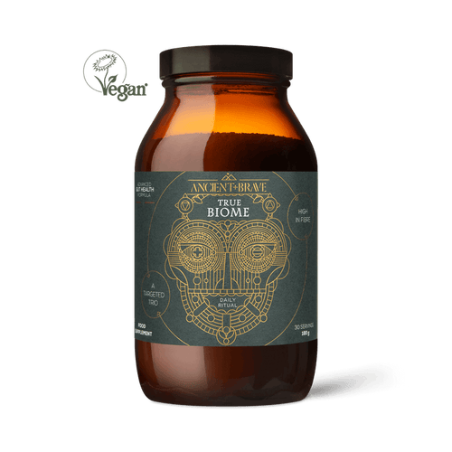 A brown glass jar labeled True Biome by Ancient + Brave, featuring a geometric face design, vegan symbol, and claims of high prebiotic fiber to support the gut barrier. The jar is displayed on a plain white background.