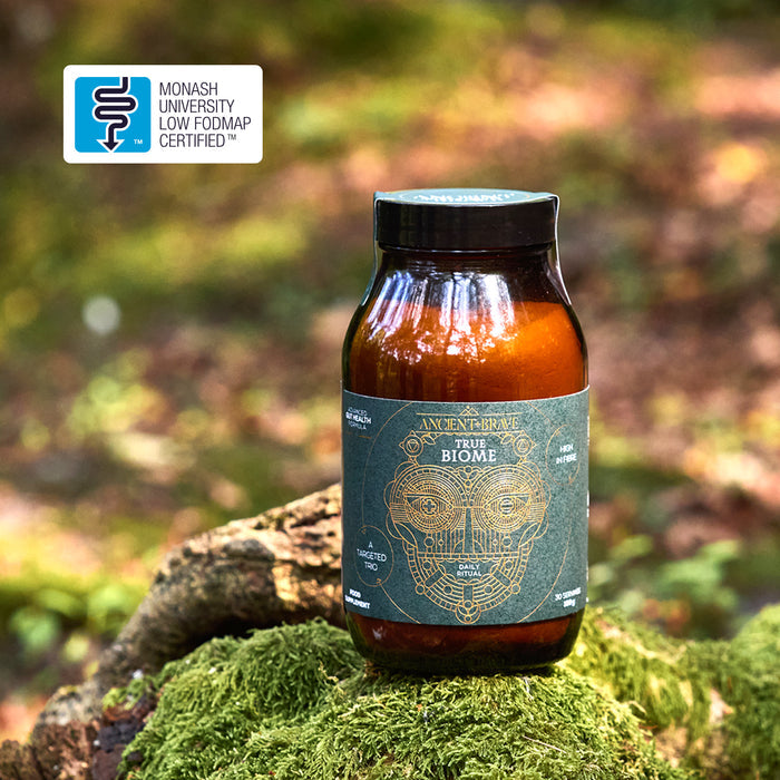 Bottle of 'True Biome' on a mossy log with a blurred natural background