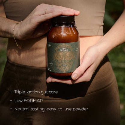 Person holding a bottle labeled 'True Biome' with text about product features including 'triple-action gut care, low FODMAP,  neutral tasting and easy-to-use powder.