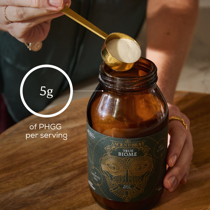 Person measuring scoop of powder from jar labeled 'True Biome' per with a focus on 5g of PHGG per serving