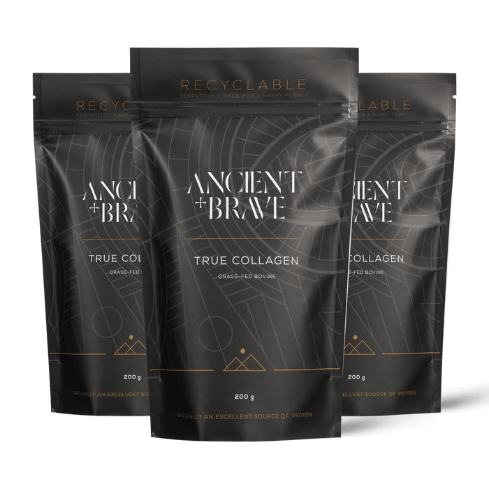 Three stand-up pouches of Ancient + Brave's True Collagen powder arranged in a fan shape against a solid black background. The packaging is dark grey with white text and gold accents.