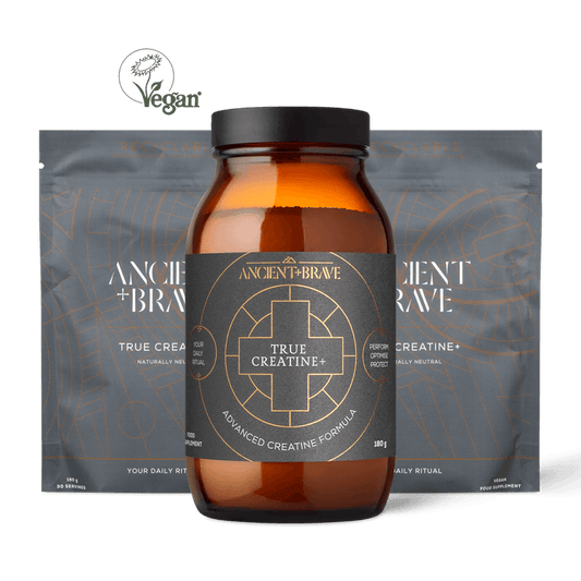 A modern, clean arrangement features a brown Ancient + Brave True Creatine+ jar in front of two sleek grey pouches from the True Creatine+ - 3 Pack. A Vegan symbol hovers above the products, highlighting their plant-based formulation for daily vitality and energy support.