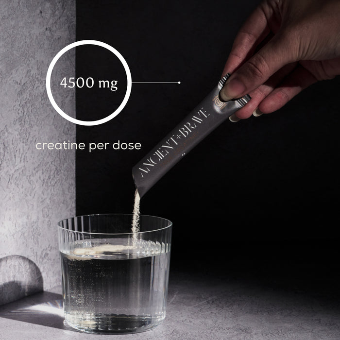 A hand pours True Creatine+ Sachets by Ancient + Brave into a glass of water, supporting energy and cognitive health. Overlay text reads 4500 mg creatine per dose against a minimalist, dark-toned background.