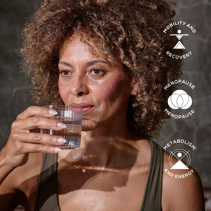 A middle-aged woman with curly hair holds a glass of water. Three icons on the right read: Mobility and Recovery, Menopause, and Metabolism and Energy—key benefits of True Creatine+ Sachets by Ancient + Brave for energy and cognitive support.