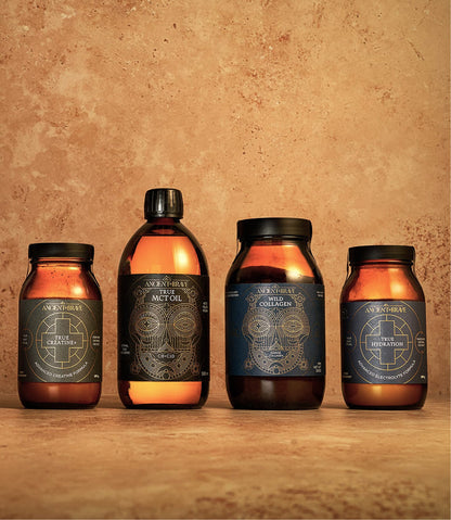 Four amber jars and bottles with intricate geometric labels from Ancient + Brave’s Ultimate Workout Kit—creatine supplement, MCT oil, collagen peptides, and hydration powder with electrolytes—are displayed against a textured, earthy brown background.