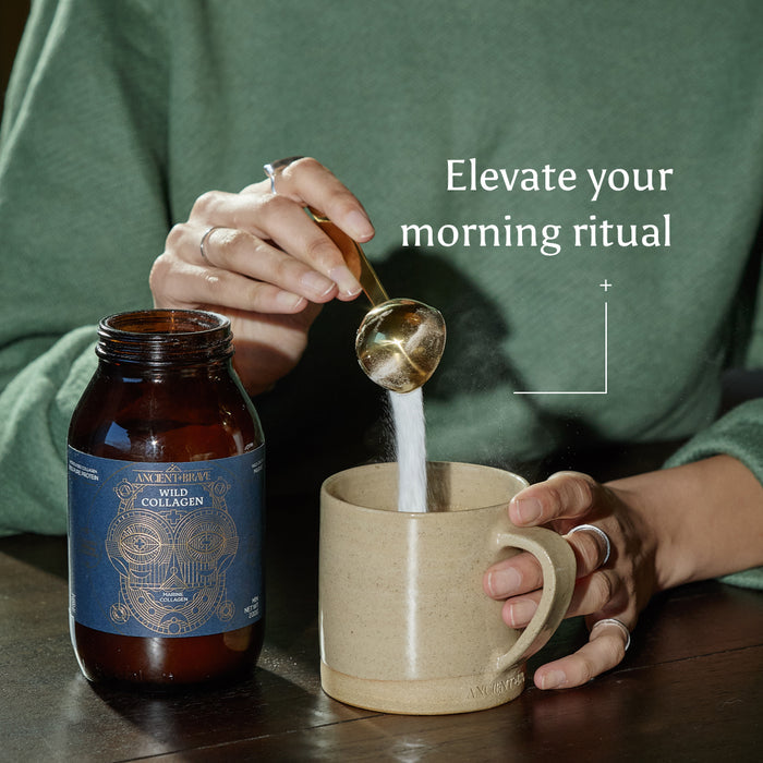 A person in a green sweater and silver rings scoops Wild Collagen into a mug. Elevate your morning ritual and wellbeing with Wild Collagen – Gift Subscription, making it easy to share this routine with loved ones.
